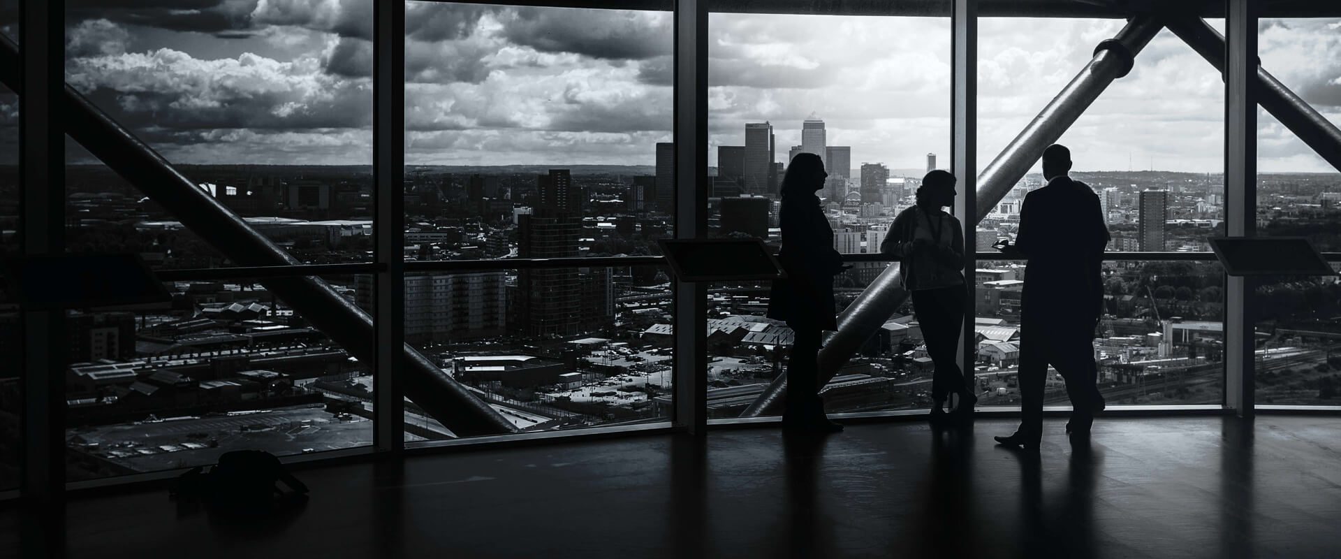 Black and white image of three people talking in front of a glass wall facing a modern city skyline.